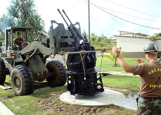 https://guernicamag.com/wp-content/uploads/2014/05/US_Navy_081017-N-1013S-001_Equipment_Operator_2nd_Class_Ted_Hillanbrand_directs_Equipment_Operator_1st_Class_Gregory_Johannsen_as_they_place_a_World_War_II_era_anti-aircraft_gun_in_front_of_the_flagpole_at_Camp_Katuu.jpg