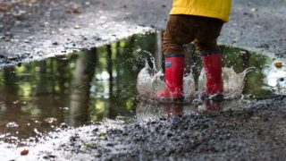 A child in red rain boots splashes around in a puddle of water.